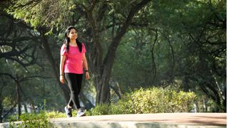 Woman walking across a path in a park in workout clothes