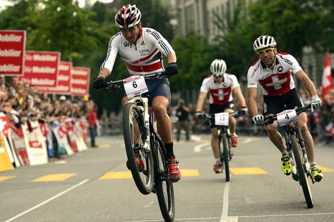 A rider does a wheelie across the line