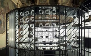 A closer look at the clock-making workshop set up in the Milan’s Palazzo Visconti. The workshop is surrounded by harsh reflector lights, while the rest of the space is dark.