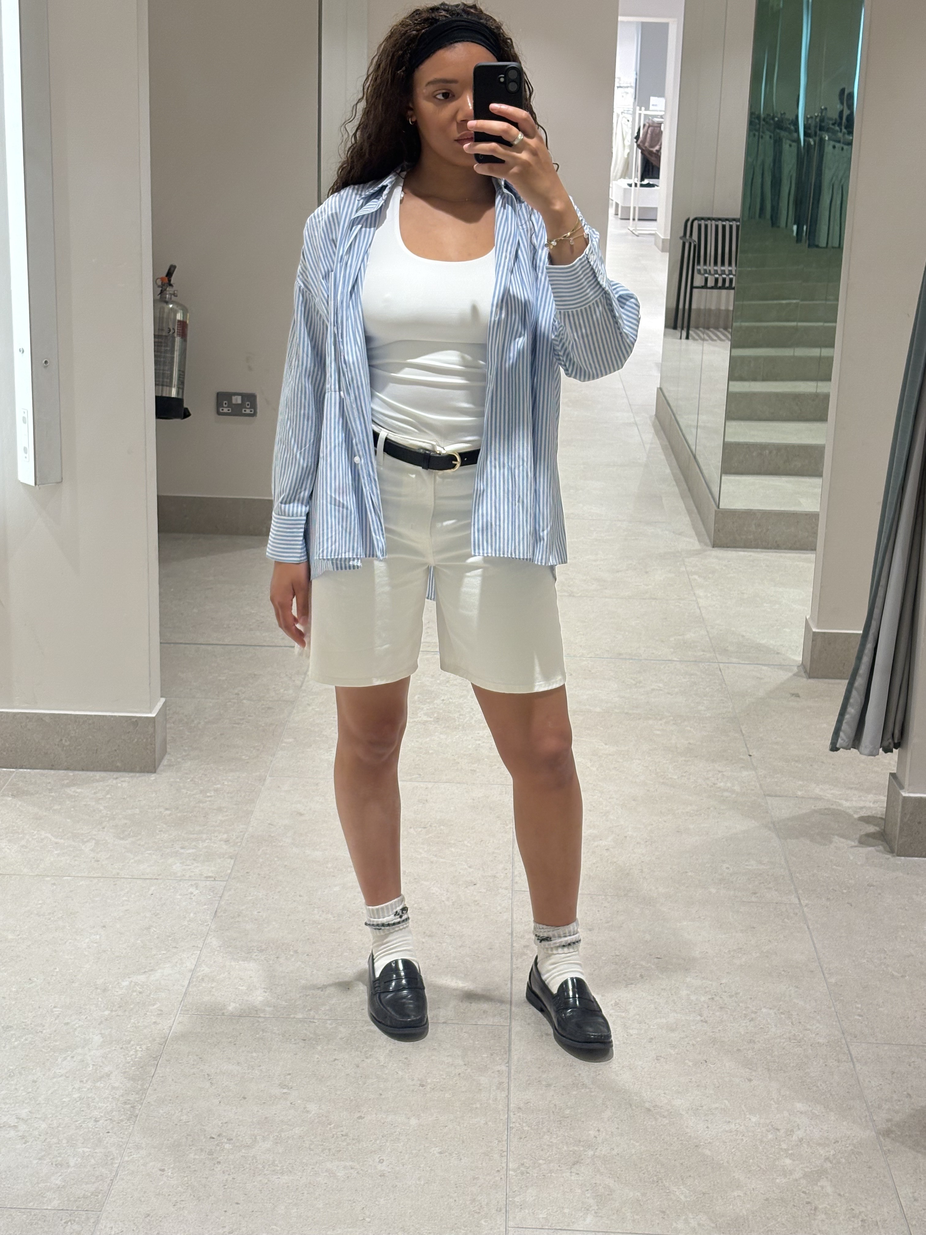junior fashion editor Imani wears white denim Bermuda shorts, a white vest top a blue and white stripped shirt and a black belt in the H&M changing rooms in a image taken recently.