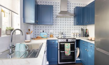 Blue kitchen with painted cabinets, chrome knobs, marble worktop, geometric tiles, wooden floor