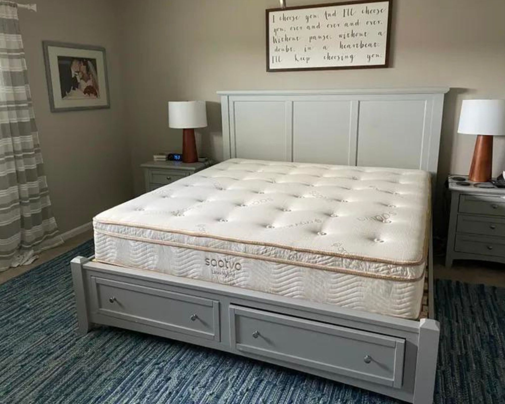 Testing the Saatva Latex Hybrid mattress on a pale grey bed in a beige bedroom with matching wooden lamps with white lampshades and a blue striped rug.