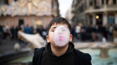 A young boy blows a bubble of gum that covers his face