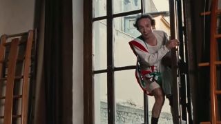 Roberto Benigni standing in a window, looking like he might jump, but smiling.