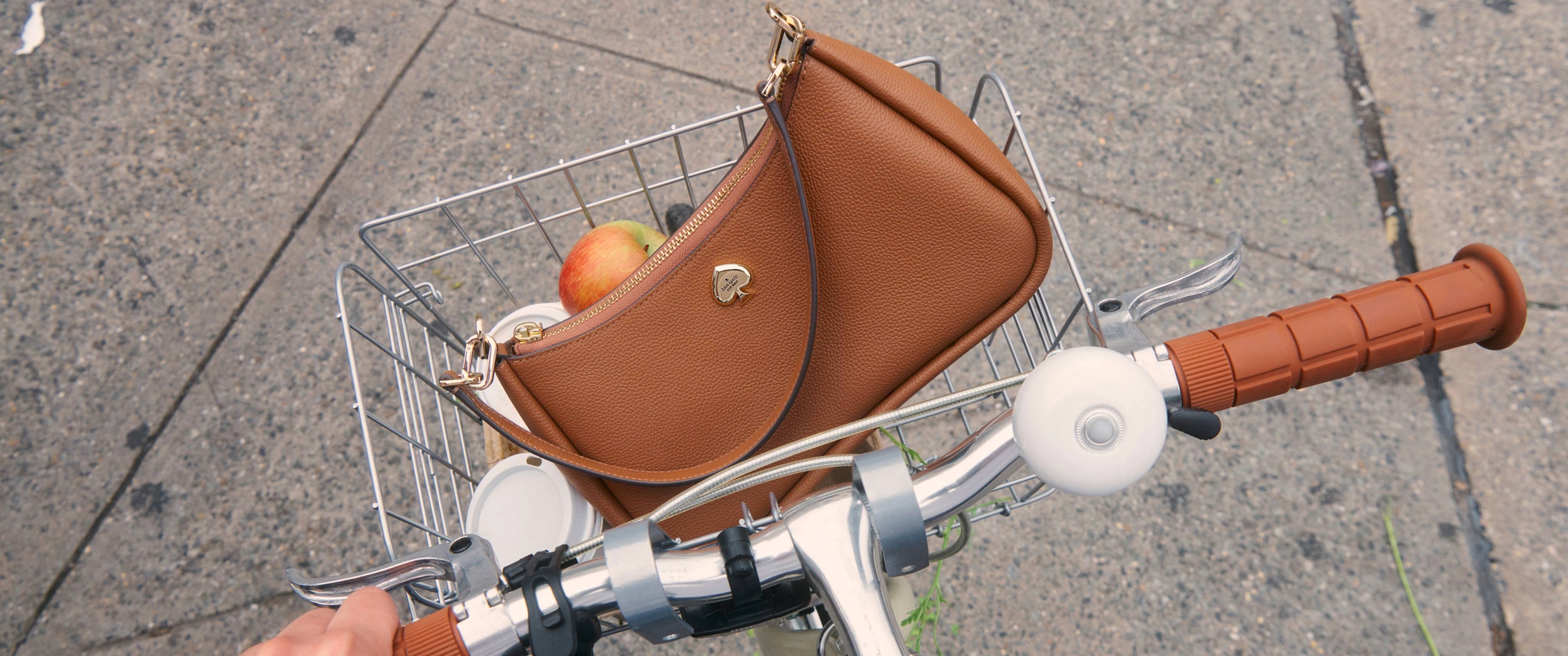 A brown Kate Spade handbag in the basket of a bike 