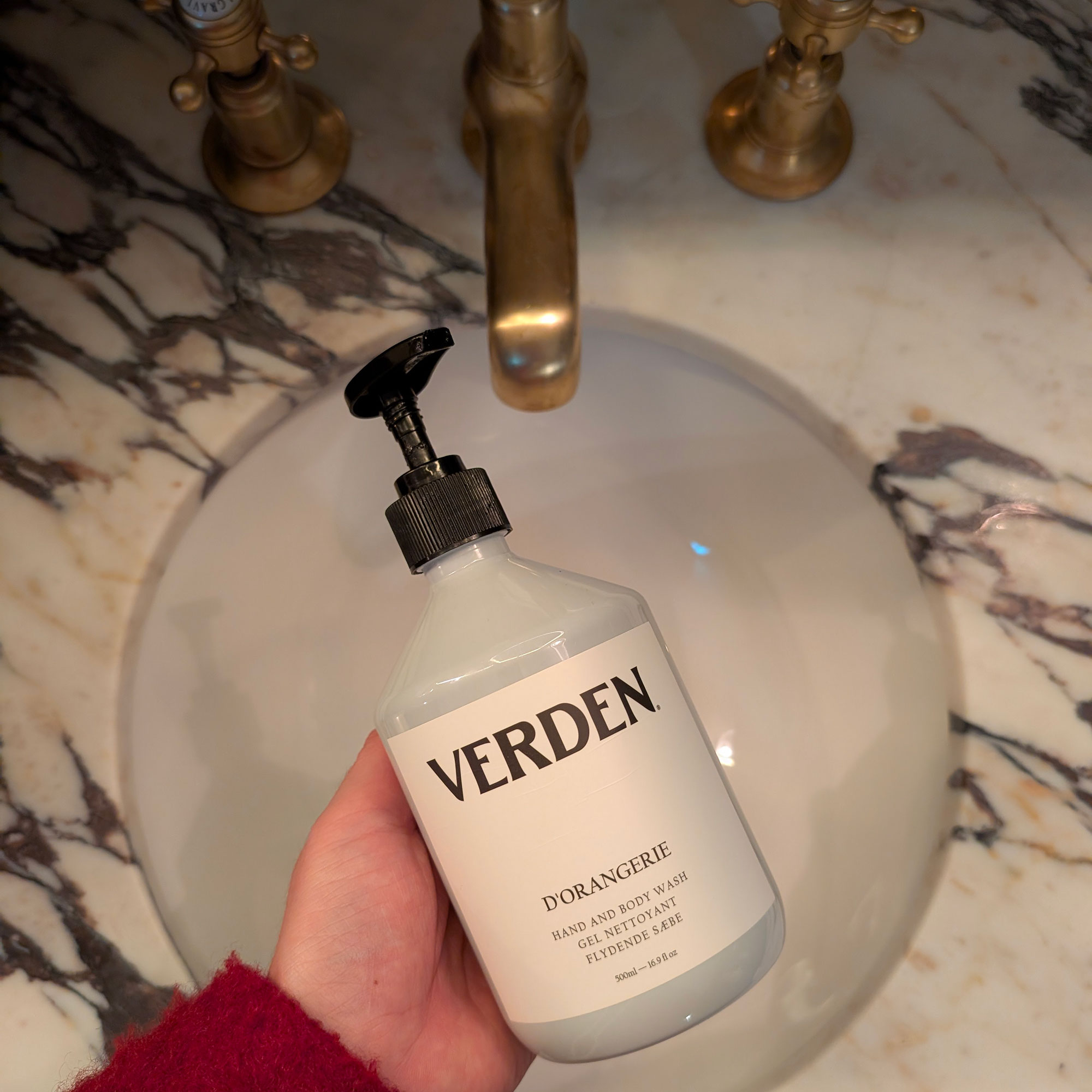 Woman holding bottle of hand soap over washbasin