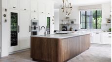 Big, dark wooden kitchen island in the centre of an otherwise all white kitchen. 