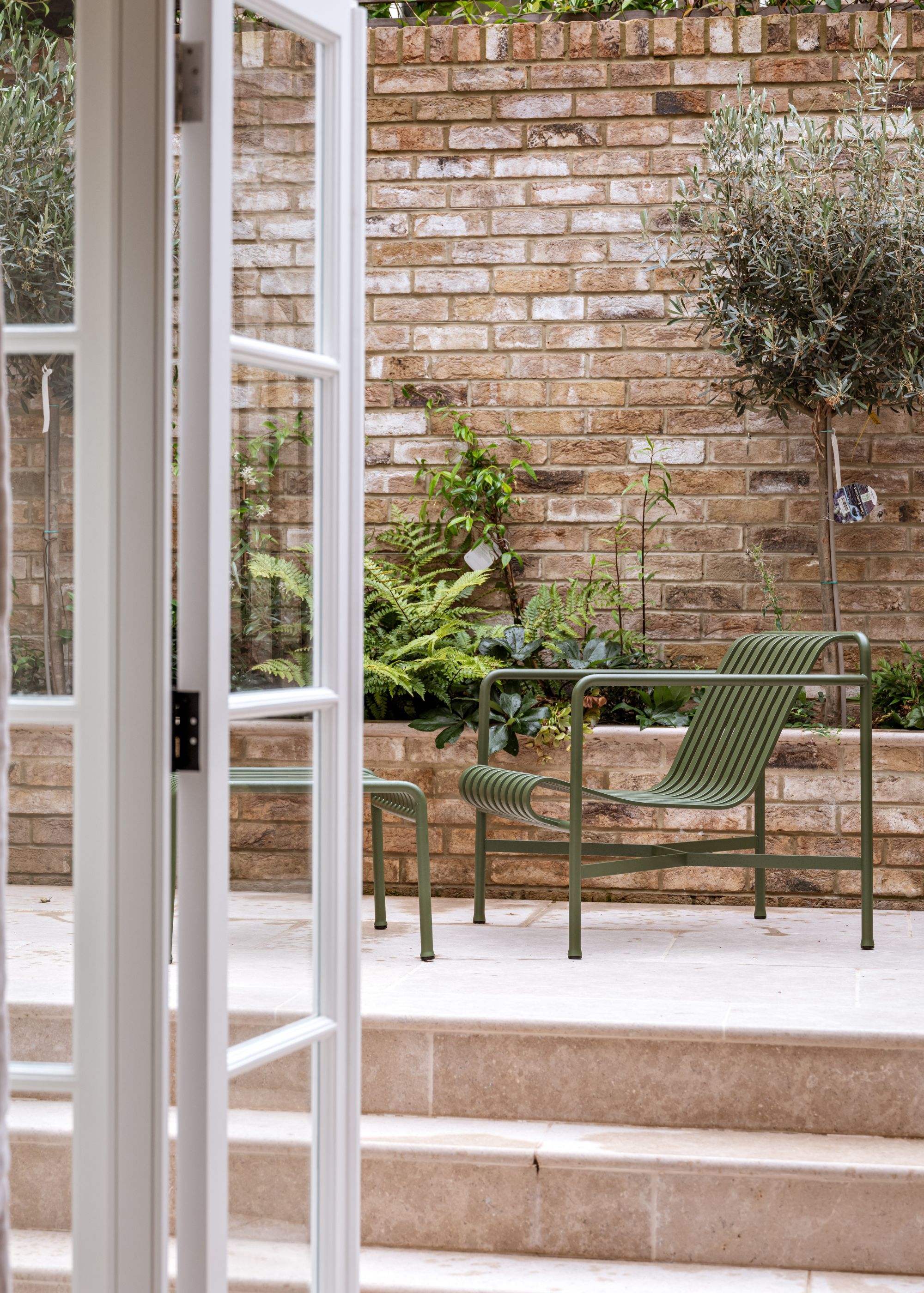 A small patio outside of a home with garden chairs and plants near the border of the patio.