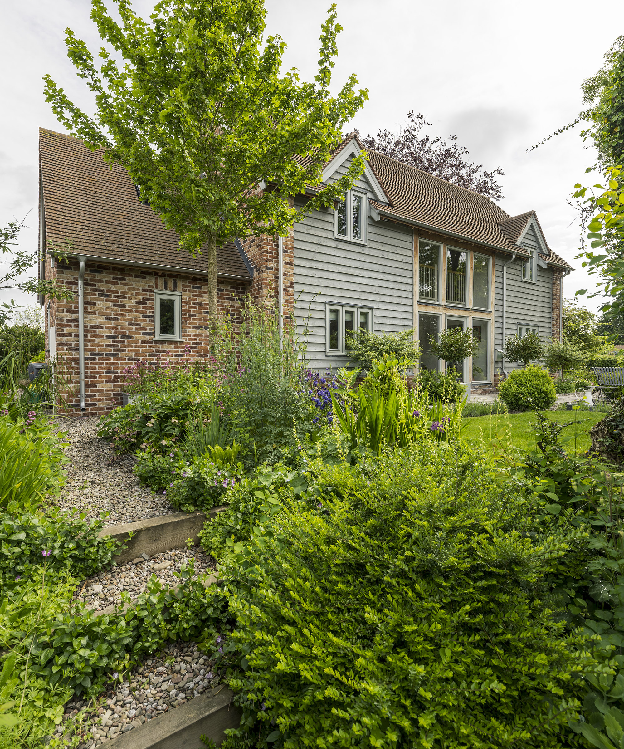 Exterior of a two storey oak frame house with brick and wood cladding with gravel garden and plants