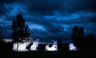 Large white nylon rabbits by Australian artist Amanda Parer with trees next to them and a cloudy evening sky above them.