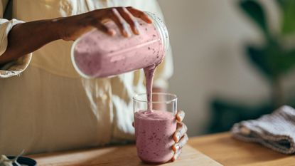 Best blenders for smoothies - A woman pouring a smoothie from the blender container into a glass on a kitchen surface