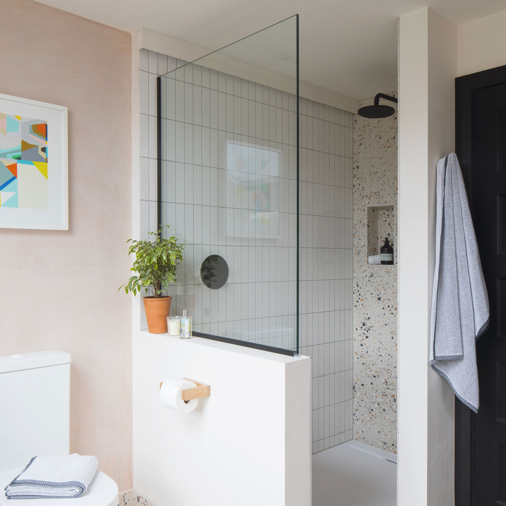 Enclosed shower with a terrazzo wall and white rectangular stacked tiles on the other wall with a black shower. A glass screen and pink walls.