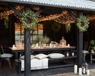 A covered seating area set for a garden party with a long table and cushions on benches
