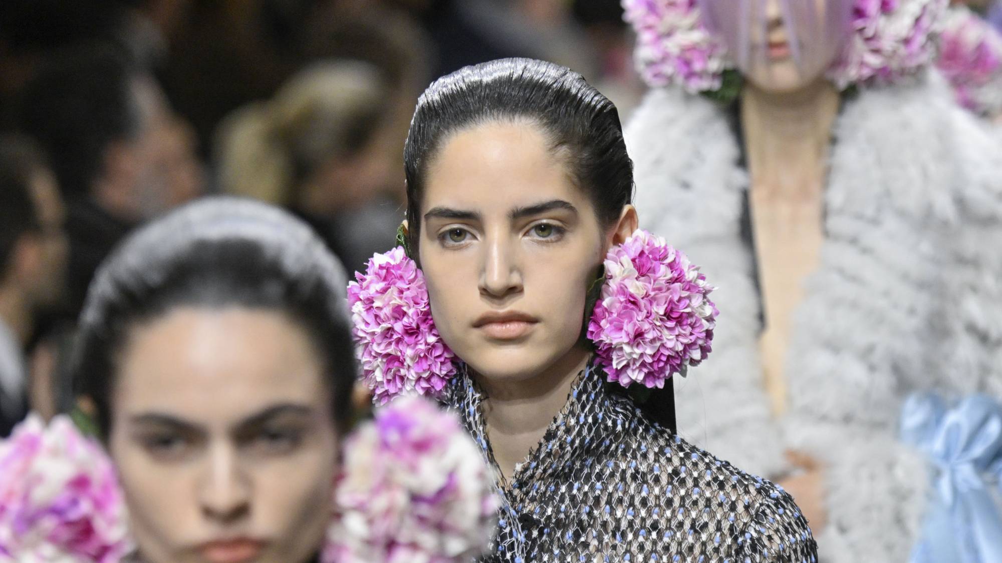 Models on a runway. Each has oversized pink and white flower earrings.