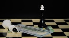 A chessboard with a hundred-dollar bill on it between the white king (on its side) and the black king.