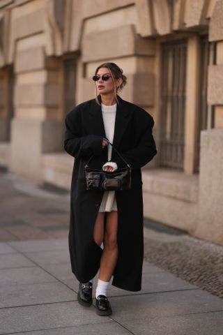 woman wearing black coat, white dress, socks, and loafers