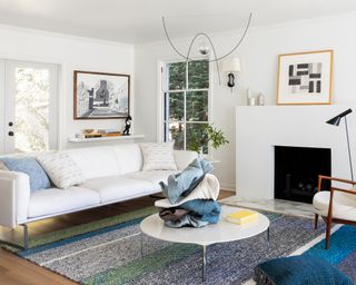 A white living room with white sofa, blue rug and art on the walls