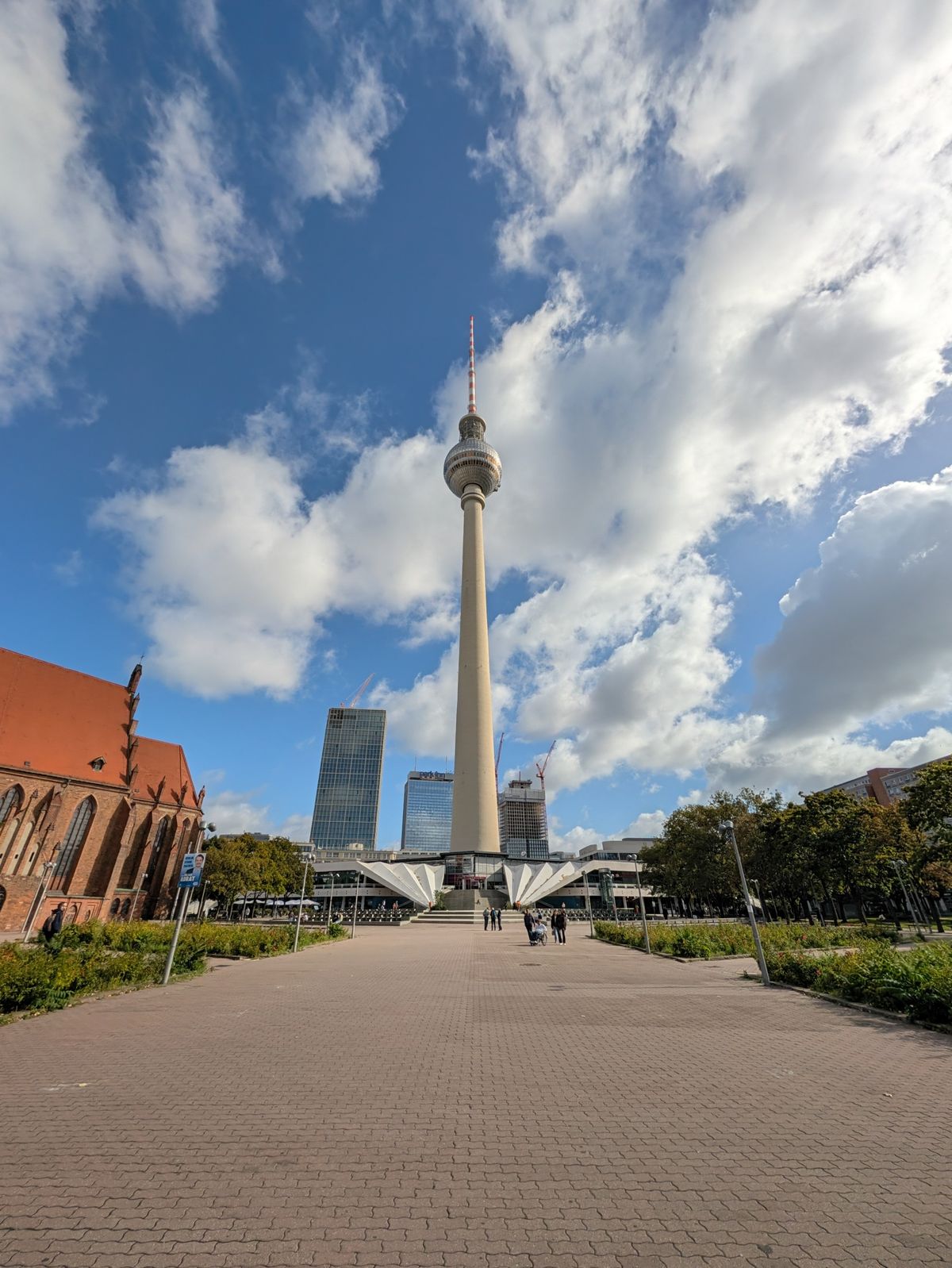 Berlin TV Tower rising above Alexanderplatz beneath a dramatic blue and cloudy sky.