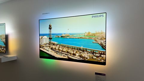 Philips OLED909 TV mounted on a white wall with an image of a Mediterranean seaside town on the screen