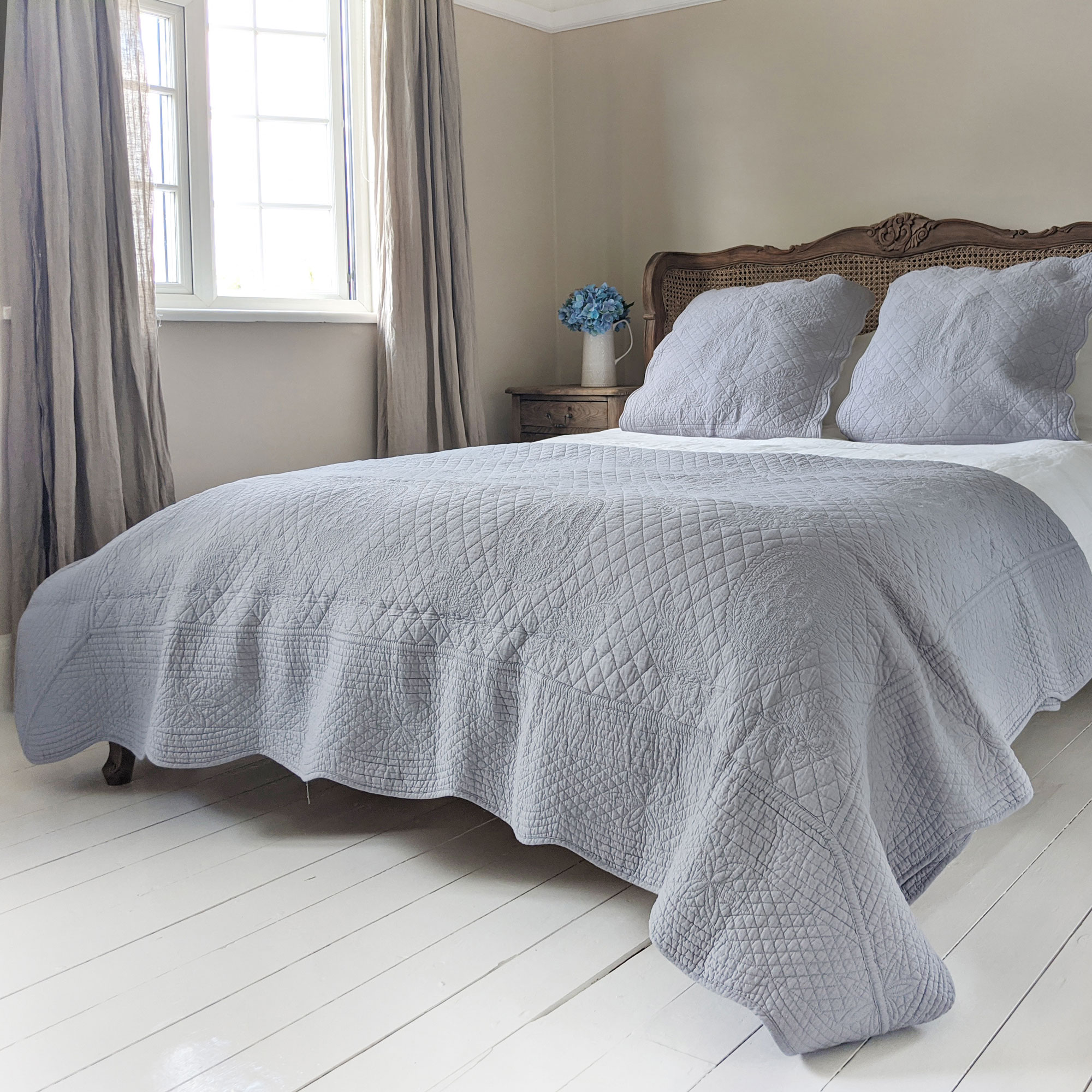 neutral bedroom with blue bedspread and grey sheer curtains
