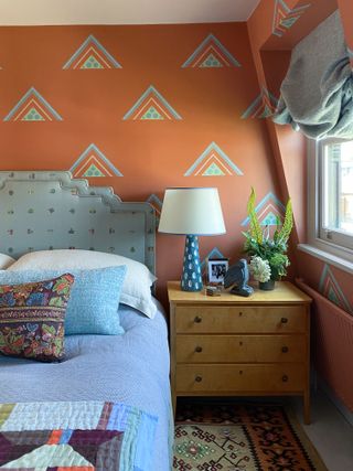 A bedroom with a rust toned wall and motifs painted on it