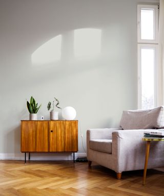 grey living space with parquet floor, grey armchair and side unit with natural light hitting wall