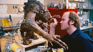 a man paints the face of a small monster puppet