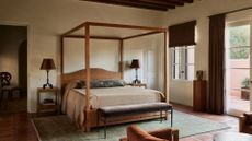 A beautiful bedroom with a wooden bed and frame, matching side tables with iron lamps, a green area rug, and a pedestal with a vase