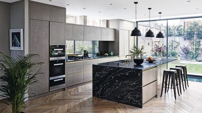 Modern fitted kitchen extension with grey wood-effect walls and black marble kitchen island on parquet floo