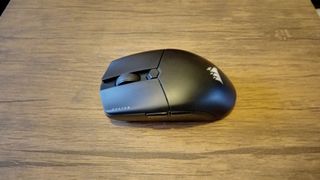 A black Corsair Katar Elite Wireless gaming mouse on a brown wooden table