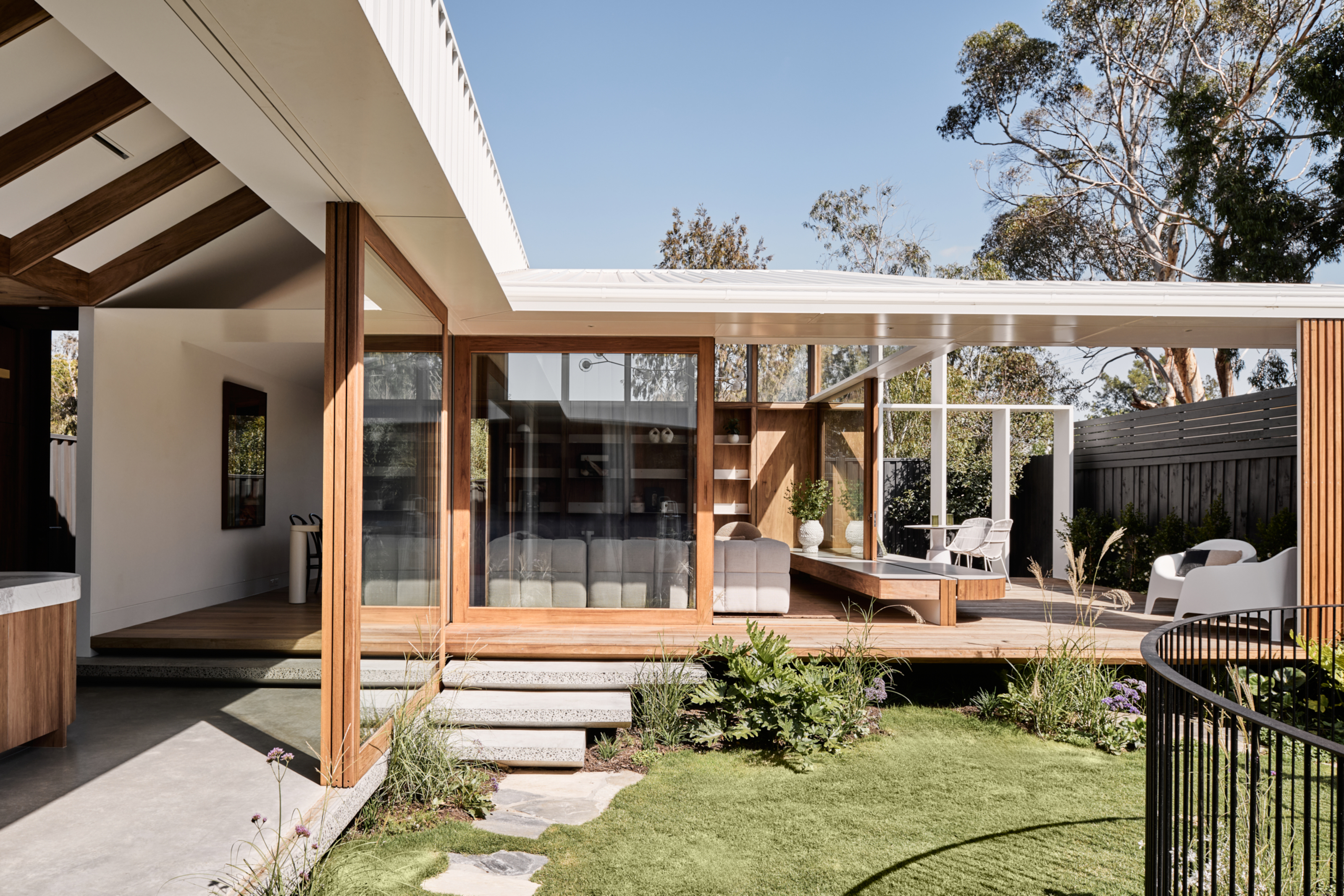 An open-plan Australian home encompassing a courtyard in the middle with a white and natural wood color scheme surrounding the grassy area in the center