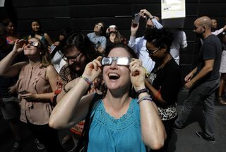 A women wearing solar viewing glasses reacts while looking at the sun during a solar eclipse near Columbus Circle in New York, U.S., on Monday, Aug. 21, 2017.