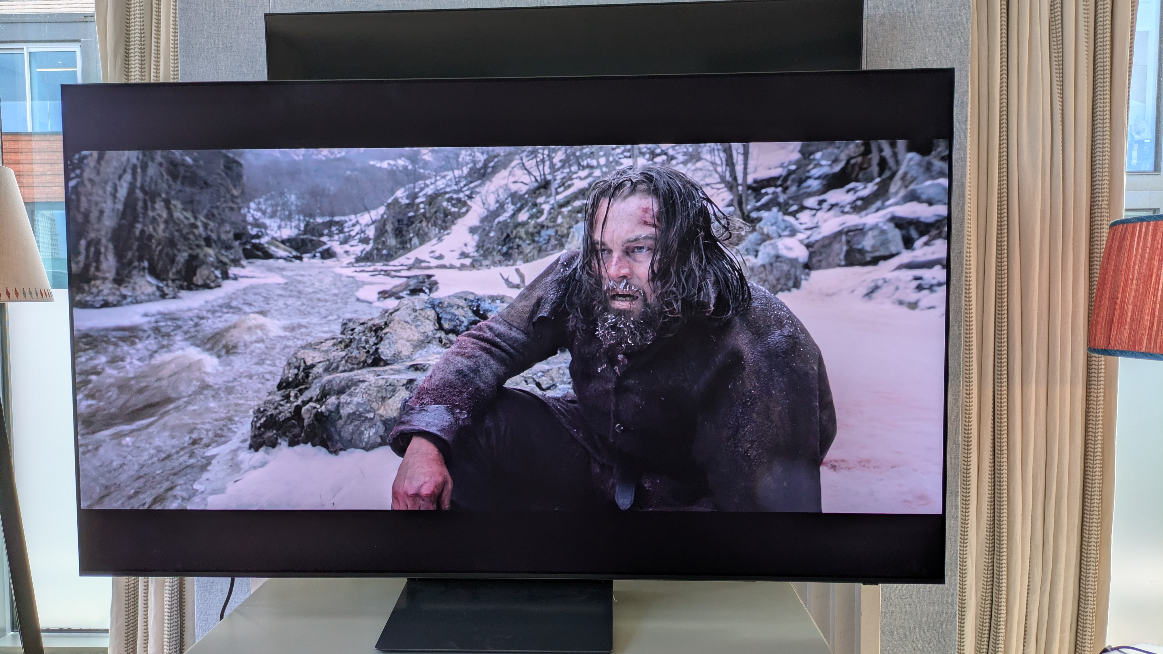 Samsung S90H OLED TV with Hugh Glass sat in snow from The Revenant