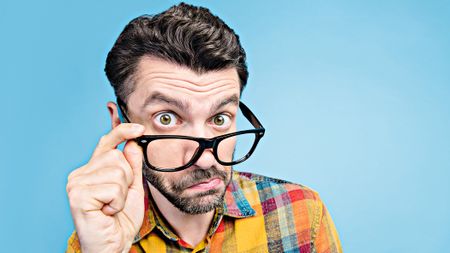 A man wearing glasses peers over them in an inquisitive manner.