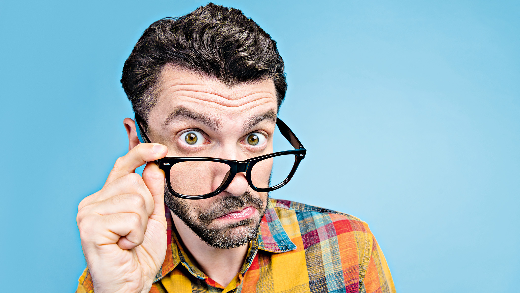 A man wearing glasses peers over them in an inquisitive manner.