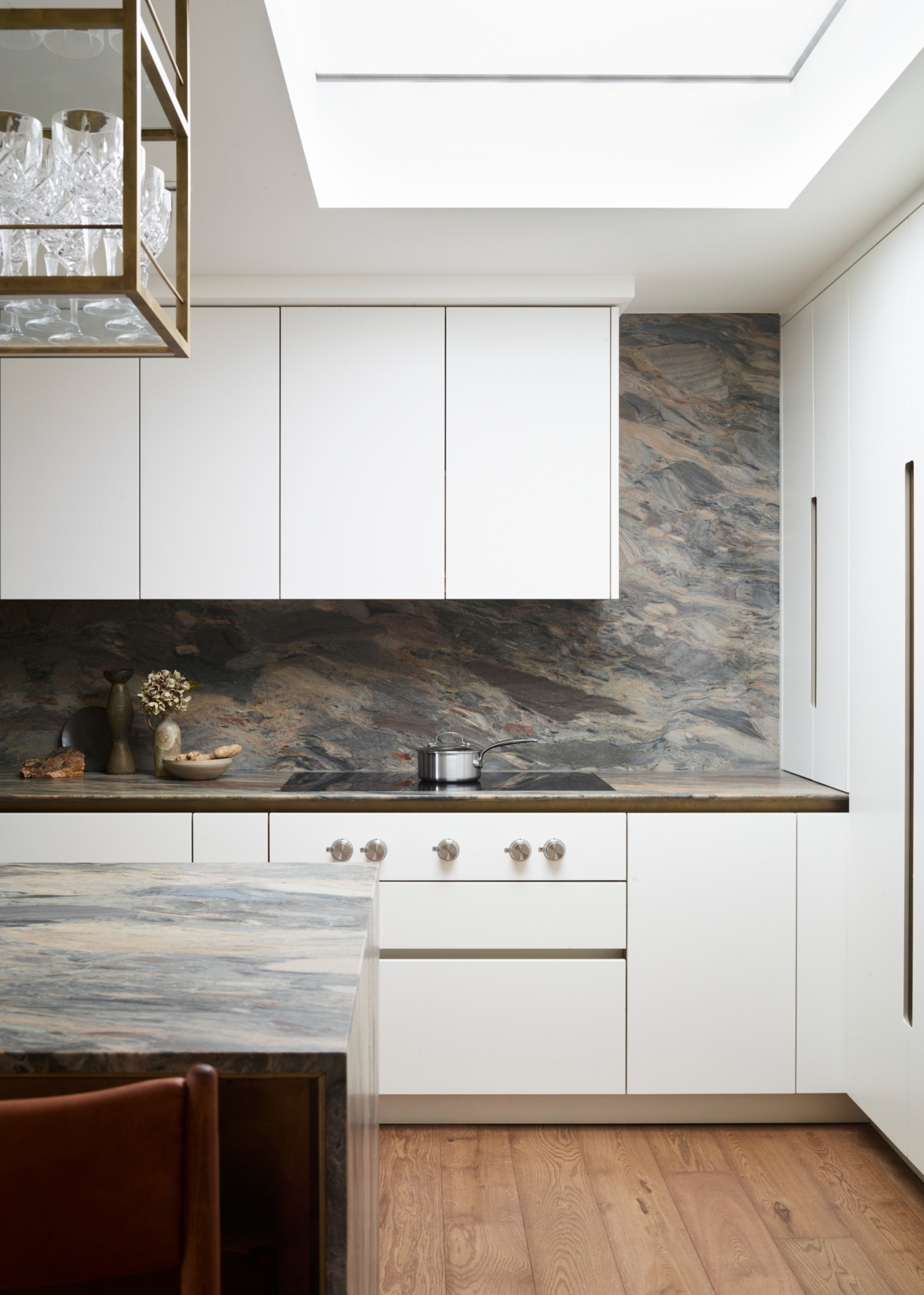 A modern white kitchen with wall cabinets and a skylight, wooden floor and a greey marble worktop
