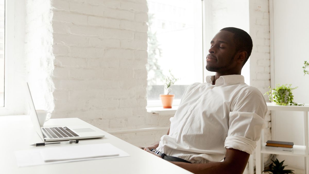 Man performing breathing exercises at desk. He is leaning back in his chair with his eyes closed.