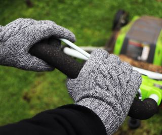 Gloved hands holding the handle of a lawnmower