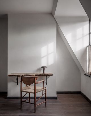 Desk attached to a white wall with a wooden chair in front of it on a wooden floor.