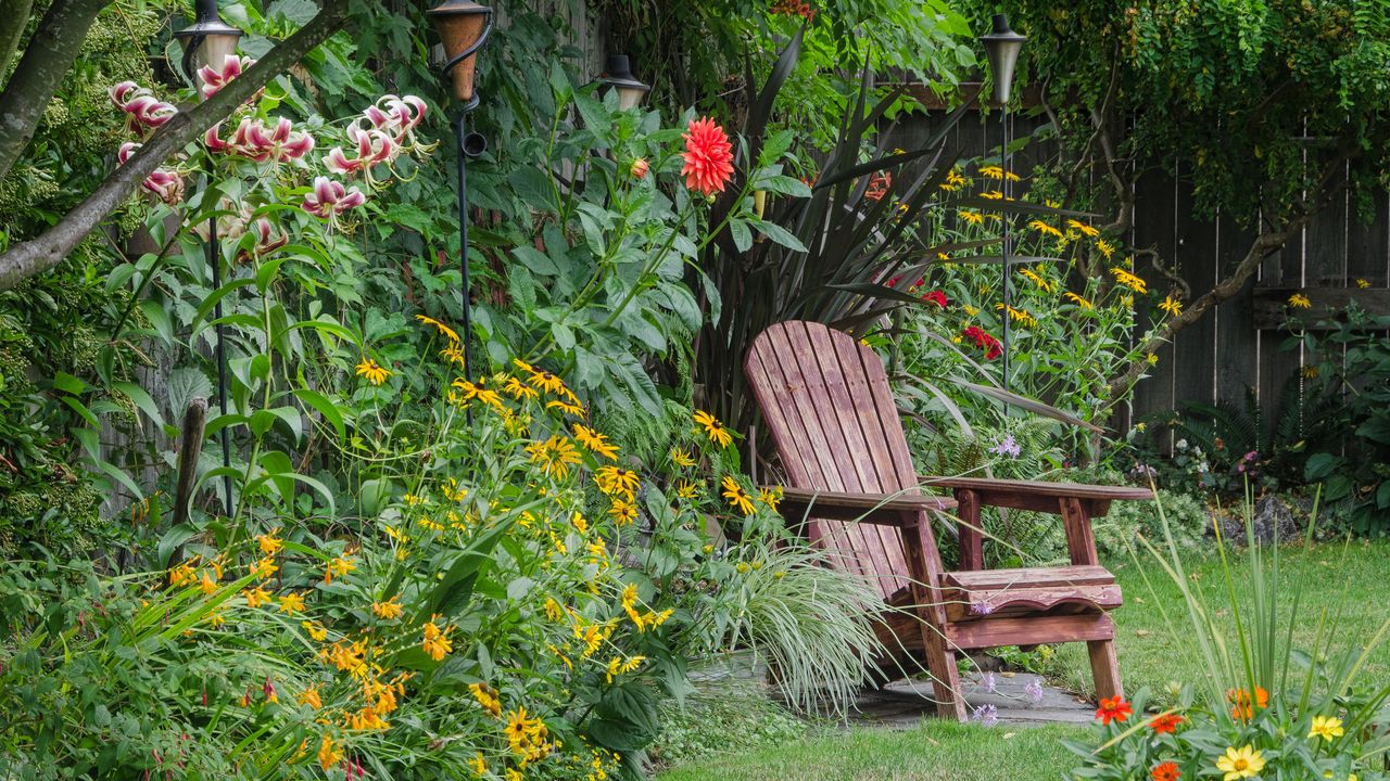 A weathered wood chair sits at the end of a stone walkway, hidden behind colorful zinnias