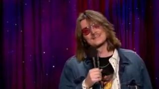 Mitch Hedberg smiling while performing standup on Late Night With Conan O'Brien