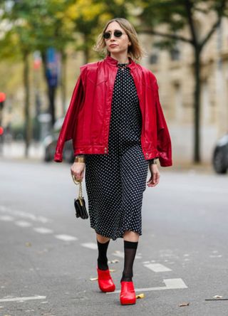 Emy Venturini wears black Rayban sunglasses, a red leather YSL jacket, a black and white Zara dress with polka dots, a black leather YSL bag with gold details, black Calzedonia socks, red leather Bottega Veneta shoes high heels, during a street style fashion photo session, on November 09, 2024 in Paris, France.