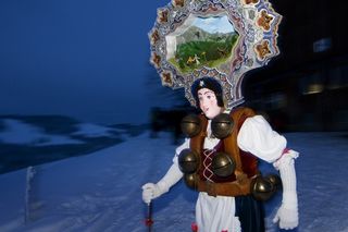 A person wearing a wooden face mask walks down a snow-covered mountain in Appenzell during Silvesterchlausen