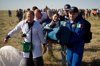Expedition 27 Flight Engineer Paolo Nespoli gives a thumbs up as he is carried in a chair to the medical tent shortly after he and Commander Dmitry Kondratyev and Flight Engineer Cady Coleman landed in their Soyuz TMA-20 southeast of the town of Zhezkazga