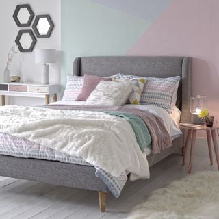 double bed with multicoloured cushions and throws on a white wooden floor with a geometric design on the wall behind