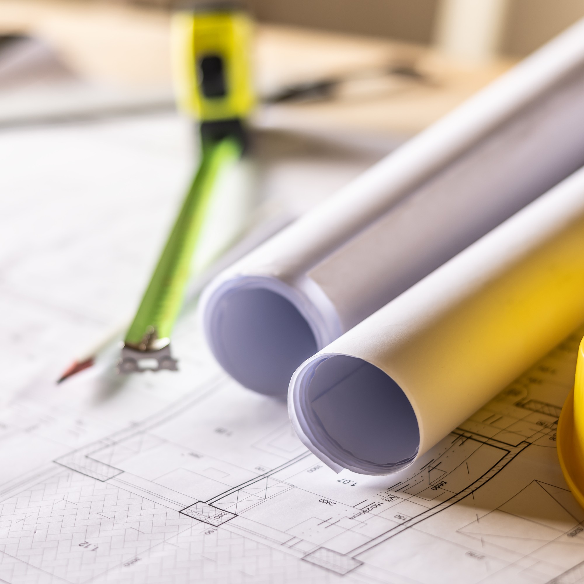 Extension plans, tape measure and yellow hard hat laid out on a table