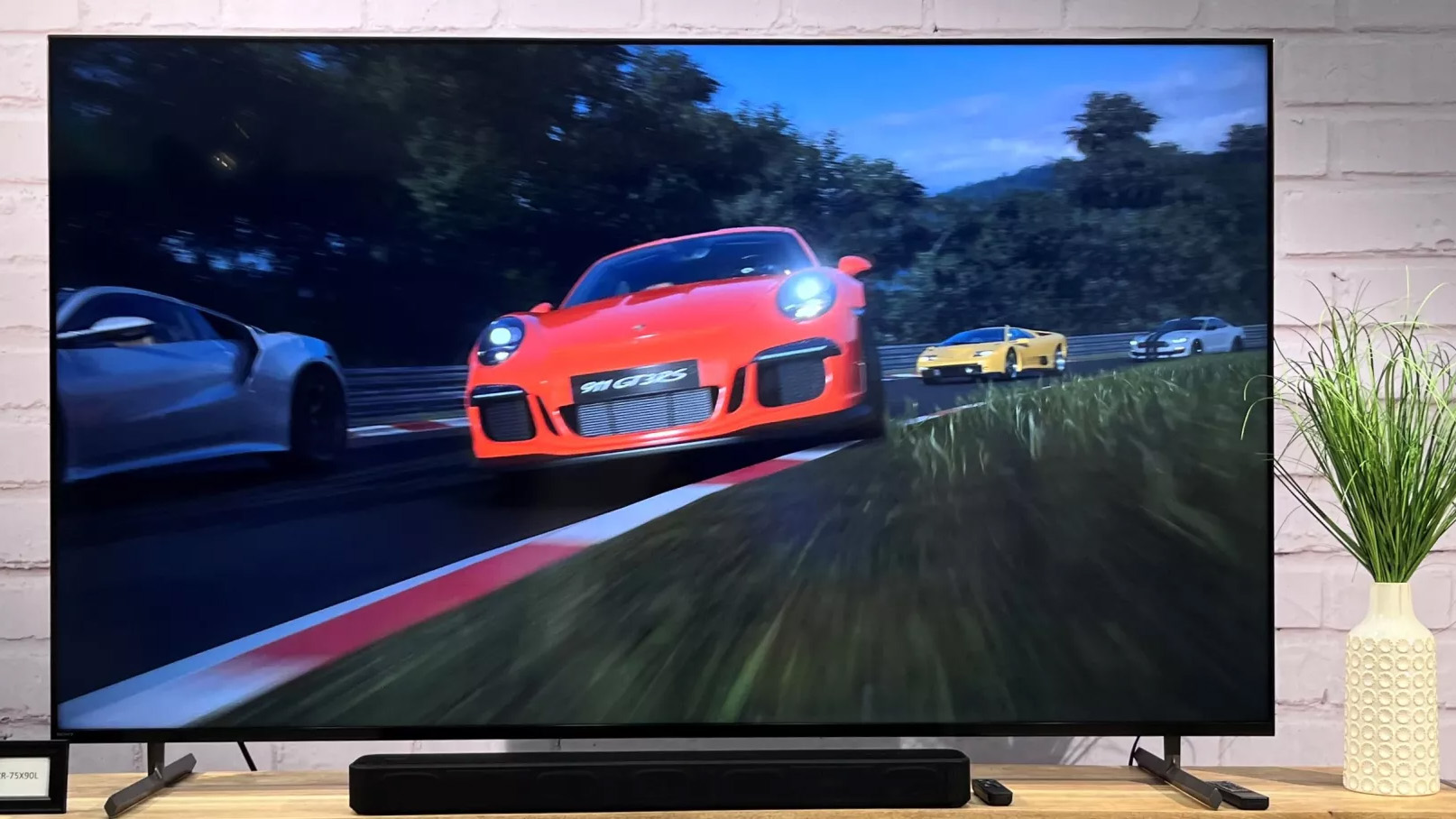 The Sony X90L LED TV pictured on a wooden shelf next to a plant displaying a game with a red car.