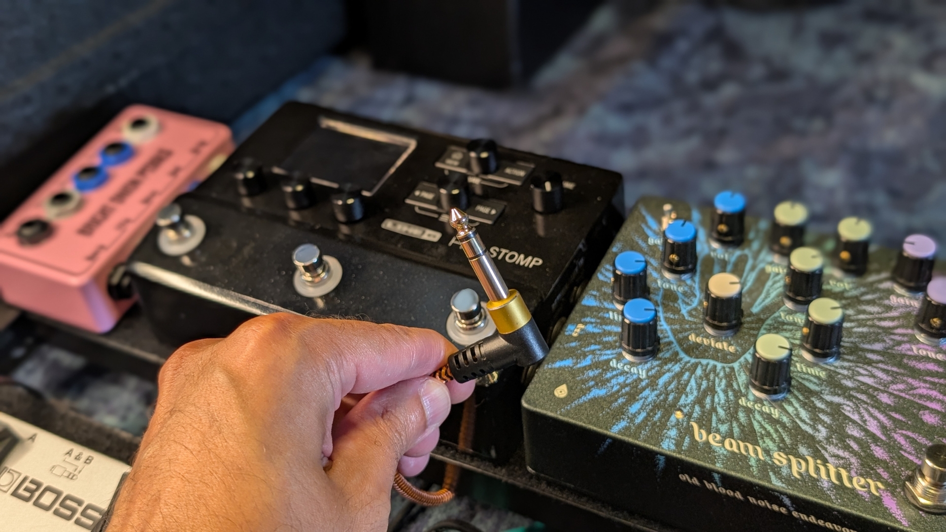 A man holds a TRS patch cable up with a pedalboard in the background