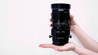 Laowa Tilt Shift lens, being held by a pair of hands against a white background