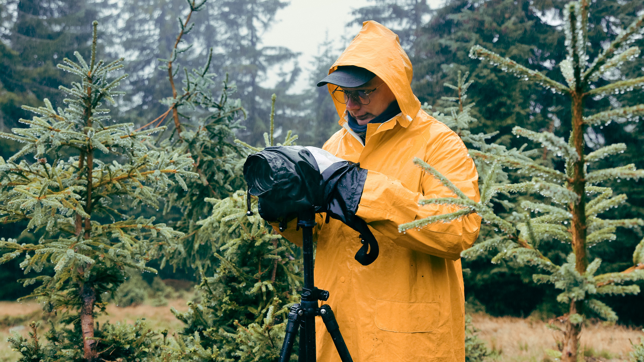 човек који носи жути кабаницу и користи камеру на стативу на киши